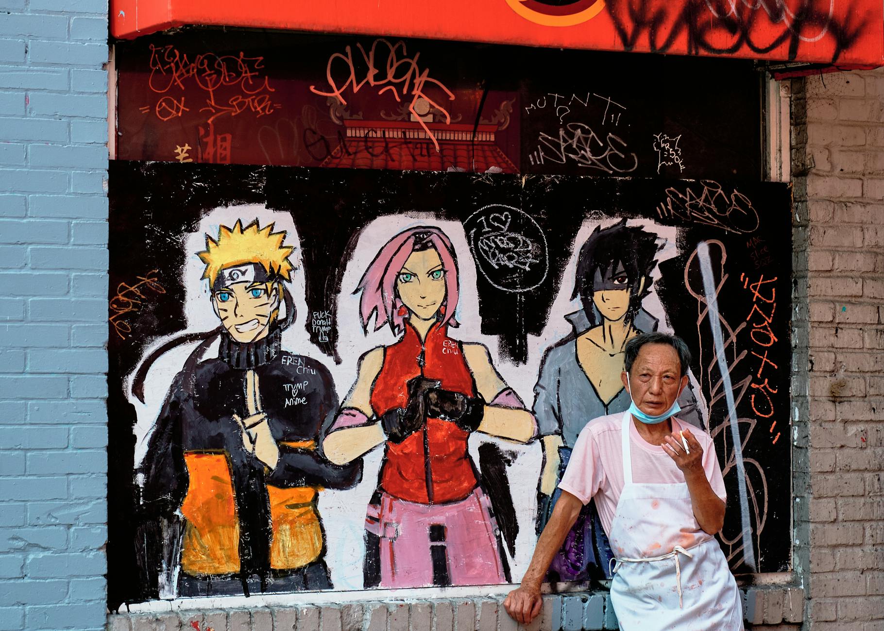 elderly man standing in front of a wall with anime paintings